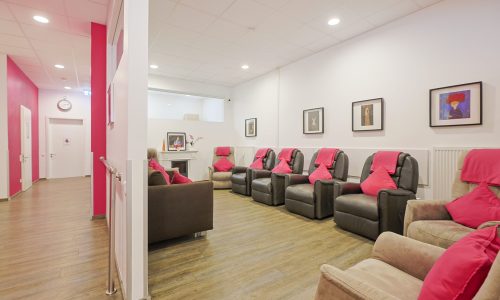 Heller Aufenthaltsraum mit Ruhesesseln, pinken Kissen und Kaminbereich; klare Orientierung und kurze Wege.